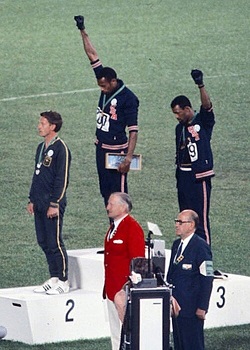 Tommie Smith (center) and John Carlos (right) and Raise Their Fists